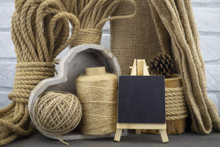 Assorted balls of hemp twine and string with skeins of rope, jute fabric and slate chalkboard in a close up rustic still lifeの写真素材