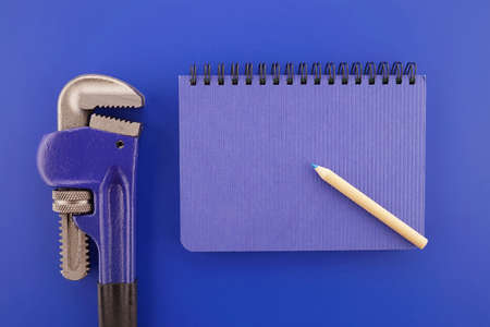 Adjustable pipe wrench and wire bound open notebook on blue background, plumbing and mechanical estimating concept with free copy space for textの写真素材