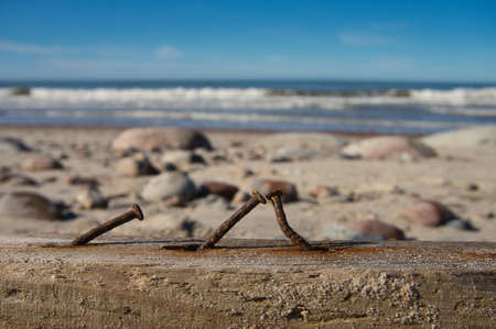 Rusty nails in a wooden railing at the seaside with a view to the tropical beach and ocean behind and selective focus to the corroded metalの写真素材