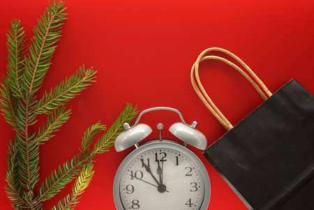 Black paper shopping bag, alarm clock and fir branch on red background with copy space for text. Black Friday sale, shopping conceptの写真素材