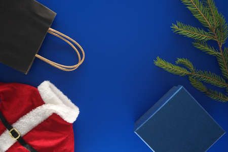 Red Santa Claus suit, black paper shopping bag, gift box and fir branch on blue background with copy space for textの写真素材