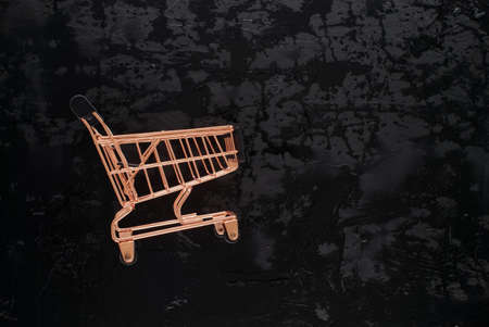 Golden shopping cart on black grunge background with copy space for text, flat lay top view template. Black Friday sale, shopping conceptの写真素材