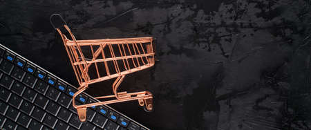 Golden shopping cart on black grunge background with copy space for text in a panoramic format to use as header or web banner. Black Friday sale, shopping conceptの写真素材