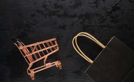Shopping cart and black paper shopping bag on black grunge background with copy space for text, flat lay top view template. Black Friday sale, shopping conceptの写真素材