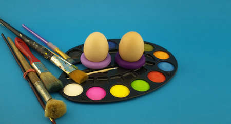Easter egg decoration concept with paint brushes and set of watercolor paints in pallet. Studio...
