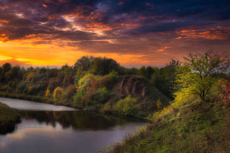 Vivid orange sunset over a tranquil river or creek in autumn with colorful fall foliage on the trees and bushes in a scenic seasonal landscapeの写真素材