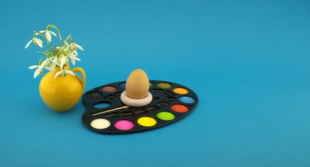 Easter egg decoration concept with set of watercolor paints in pallet, next to a yellow jug with...