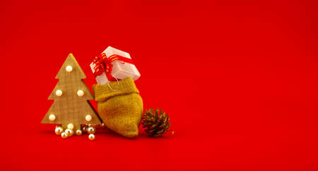 Stylized wooden Christmas tree and jute sack with gift boxes on a festive red background. New Year and Christmas gift season conceptの写真素材