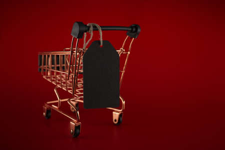 Black sale tag and golden shopping cart over red background with copy space for text. Black Friday sale, shopping conceptの写真素材
