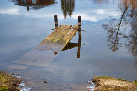 Spring flooding, old broken sunken jetty in a tranquil lake with reflections on the waterの写真素材
