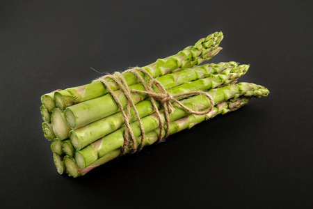 Fresh bunch of green asparagus tied with jute cord over a black background. Spring vegetable, eco friendly packagingの写真素材
