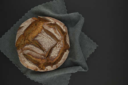 Bread loaf on a gray kitchen towel placed on a black table, top view with copy space
