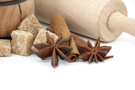 Brown cane sugar cubes in wooden sugar bowl next to cinnamon sticks, star anise and rolling pin. Confectionery concept isolated on white backgroundの写真素材