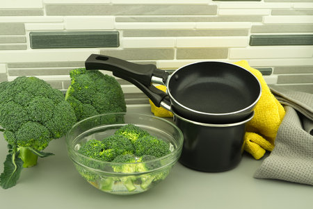 Fresh broccoli florets soaked in a clear bowl of water next to the pan and pot. Fried or boiled conceptの写真素材