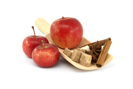 Cinnamon sticks, brown sugar cubes and anise stars placed in wooden scoop near red applesの写真素材