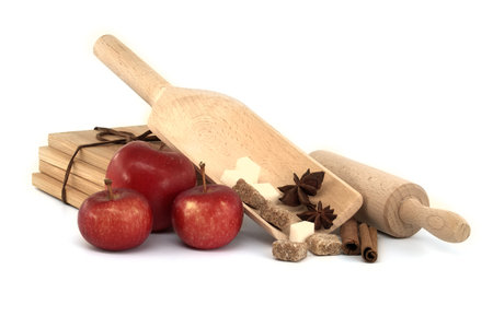 Cinnamon sticks, brown sugar cubes and anise stars placed in wooden scoop near red apples and rolling pinの写真素材