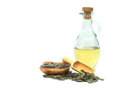 Dried hulled pumpkin seeds in wooden scoop and pumpkin oil in glass decanter isolated on white backgroundの写真素材