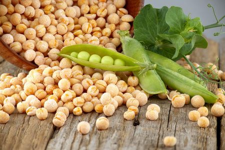 Whole dry yellow peas spilling from a rustic bowl and fresh plant with pods on rustic wood tableの写真素材