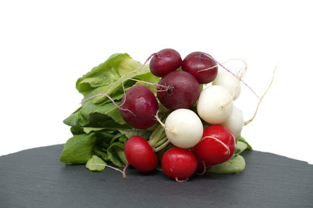 Radish with leaves on black slate serving bosrd over white background. European radishes (Raphanus sativus)の写真素材