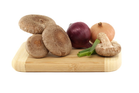Shiitake mushrooms and various kinds of onions on a wooden cutting board over on white background. Recipes and medicinal herbsの写真素材
