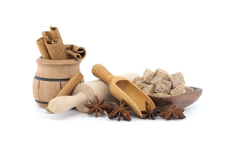 Wooden scoop with star anise with a seed inside, cinnamon sticks and brown sugar cubes in a wooden bowl near rolling pinの写真素材