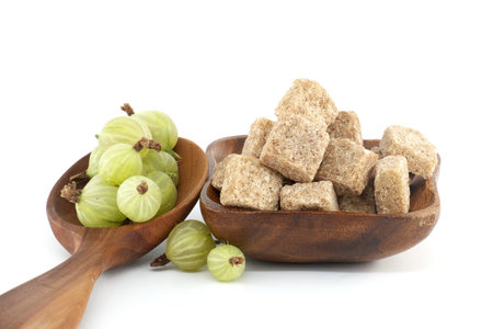 Green ripe gooseberries in a wooden spoon next to brown cane sugar cubes in wooden bowl, canning food preservationの写真素材