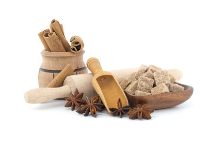 Wooden scoop with star anise, cinnamon sticks and brown sugar cubes in a wooden bowl near rolling pinの写真素材