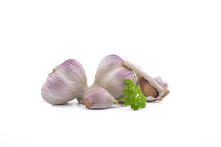 Garlic bulbs, cloves and green parsley twig in close-up isolated on white backgroundの写真素材