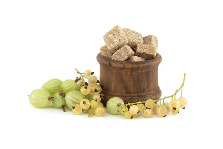Gooseberries and yellow currants next to brown cane sugar cubes in wooden bowl, isolated on white background, berry jam, compote preparationの写真素材