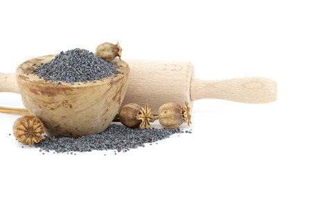 Poppy seeds in wooden bowl and seed pods in front of the rolling pin isolated on white background, full depth of fieldの写真素材