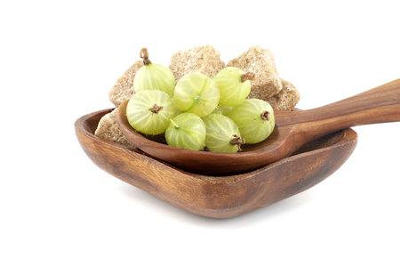Green ripe gooseberries in a wooden spoon next to brown cane sugar cubes in wooden bowl, canning food preservationの写真素材
