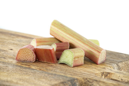 Group of rhubarb pieces in various shapes and sizes arranged in a scattered formation on wooden cutting board isolated on white backgroundの写真素材