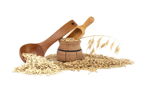 Oat grains with hulls or husks spilling from a wooden barrel and oats groats rolled and flattened into flakes in wooden spoon isolated on white backgroundの写真素材