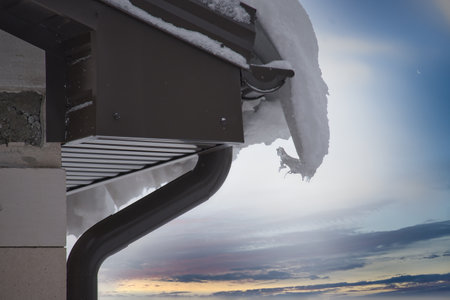 Detailed view of a snow-covered gutter on the left side of a roof, filled to a significant extent with snow, even nearing the roof's edgeの写真素材