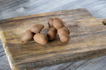 Rustic scene of a group of brown sweet tamarind fruits spread across a wooden surface with different shades of greyの写真素材