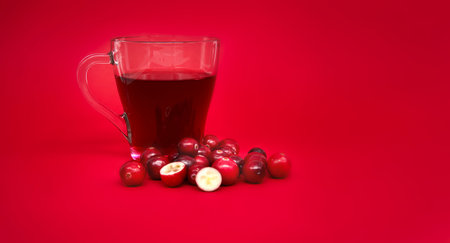 Red cranberries and transparent cup containing a dark red cranberry juice against a vibrant red backgroundの写真素材