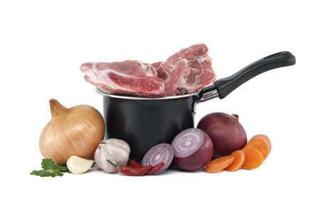 Black saucepan with pieces of raw pork inside. Around the saucepan are sliced vegetables which include onions, carrots, and garlic isolated on white background. Preparation of meat brothの写真素材