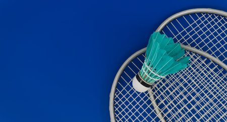 Yellow badminton feather shuttlecock on badminton racket over a blue background, banner size image with copy spaceの写真素材