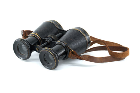 A pair of antique black binoculars with brown leather straps is showcased against a white backgroundの写真素材
