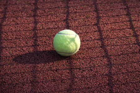 Yellow tennis ball is resting on a tennis hardcourt surface, empty court with no players, equipment or any notable activity presentの写真素材