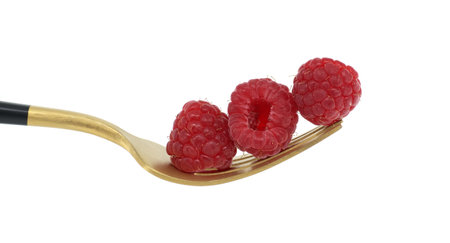Red raspberries neatly stacked on the prongs of a gold fork with a black handle isolated on a white background, Healthy diet, organic food conceptの写真素材