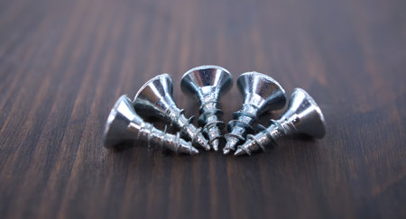 Close-up of five silver screws on a wooden surface, illustrating industrial design and metal craftsmanship for hardware projects.の写真素材