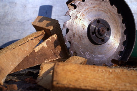 Close-up of a rusted circular saw blade slicing through wooden logs, surrounded by wood shavings and debris on the workshop floor.の写真素材