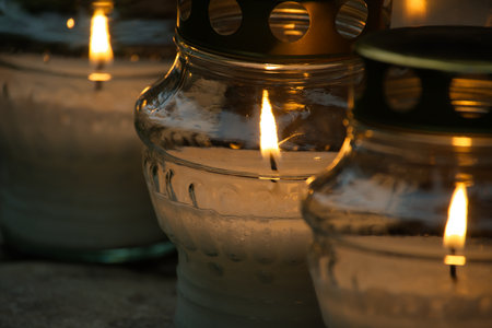 Close-up of burning candles in glass jars creating a warm and peaceful glowing light. Ideal for concepts of serenity, memorial, meditation, and relaxation.の写真素材