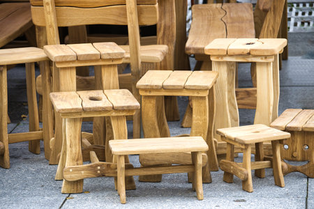 A variety of handcrafted wooden stools and benches arranged outside, highlighting rustic design and...