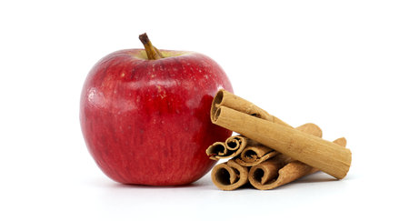 A vibrant red apple paired with aromatic cinnamon sticks, showcasing a classic combination of fresh, natural ingredients on a clean white backgroundの写真素材
