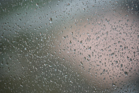 Close up of a window glass surface with water droplets against a blurred background creates a...