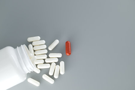 Overturned white medicine bottle with its contents white pills or capsules, spilled out onto a gray...