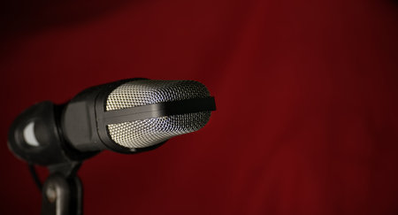 Professional studio microphone with metal mesh grille against dark red background, ideal for music recording, podcasting, and broadcastingの写真素材