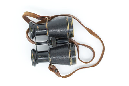 Ancient pair of black binoculars with brown leather straps isolated on white backgroundの写真素材